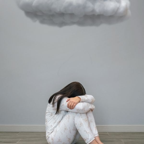No_motivation Young lady in pajamas sitting under a cloud indoors