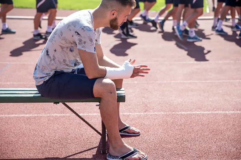 Sports_Athlete_injury (1) An injured athlete sitting on the bench, while other sport athlete compete